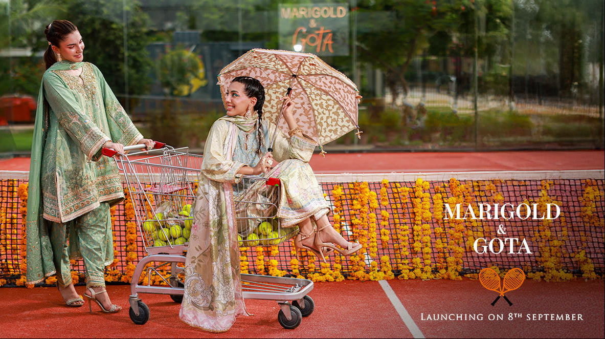 Two women in traditional attire with a shopping cart and umbrella on a red carpet, with 'Marigold & Gota' branding.