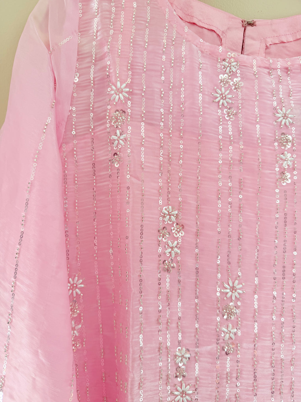 Close-up of a pink fabric with silver sequin and floral patterns on a light green background