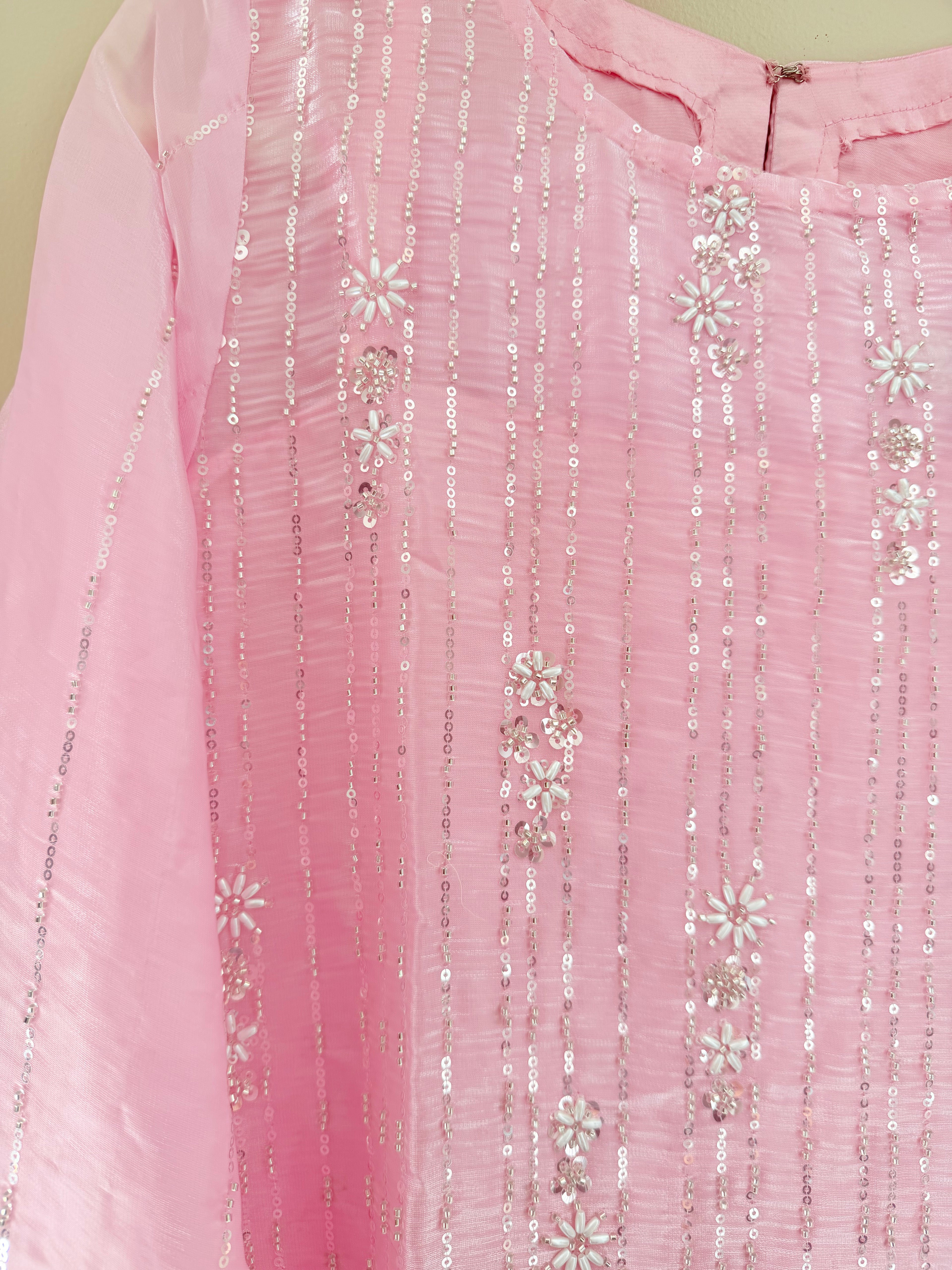 Close-up of a pink fabric with silver sequin and floral patterns on a light green background