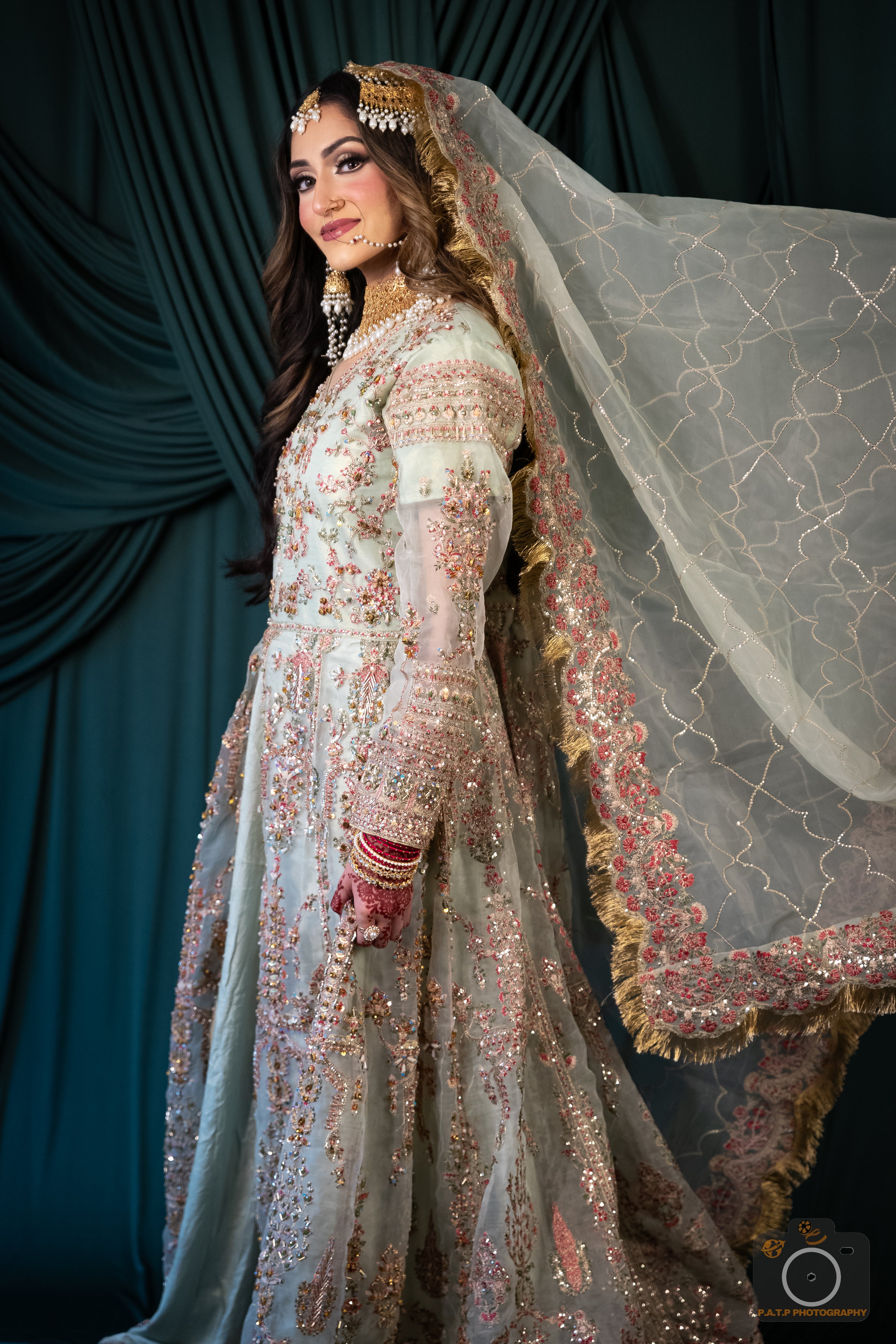 Woman in a traditional embroidered outfit with a veil against a dark curtain background