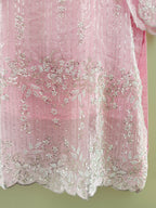 Pink fabric with intricate white embroidery on a green background
