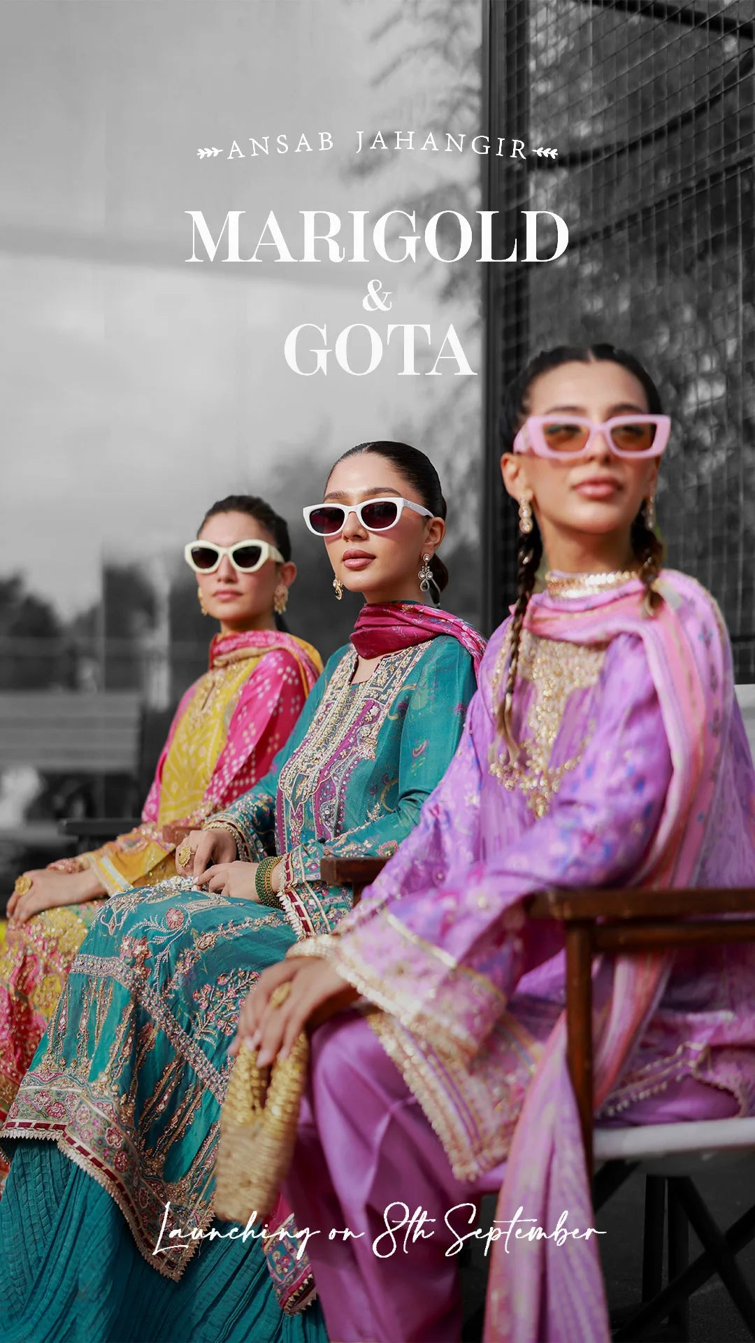 Three women in colorful traditional outfits with sunglasses, sitting outdoors.