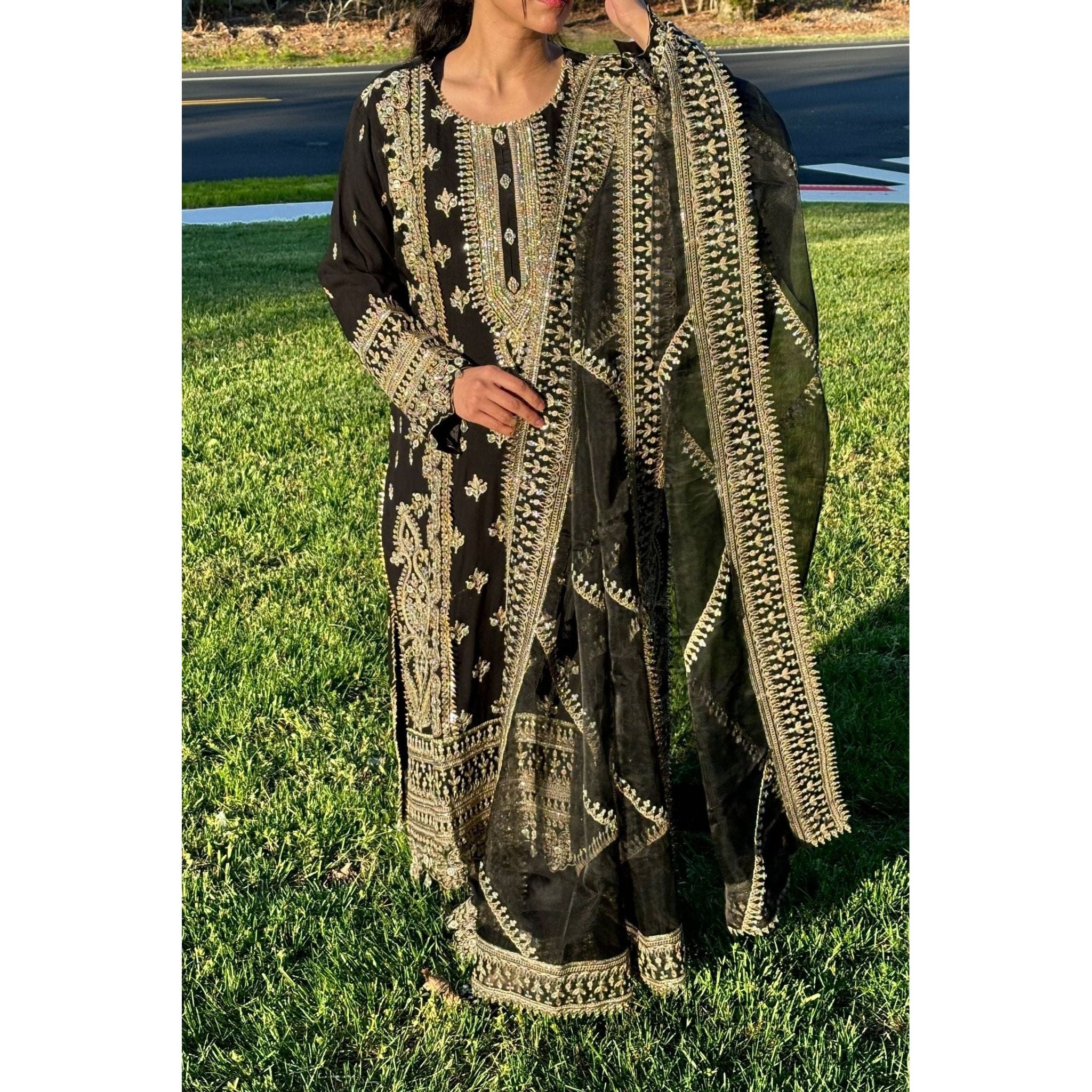 A stunning black suit adorned with beige and gold embroidery, complemented by a dupatta and plazzu pants also embroidered with intricate designs.