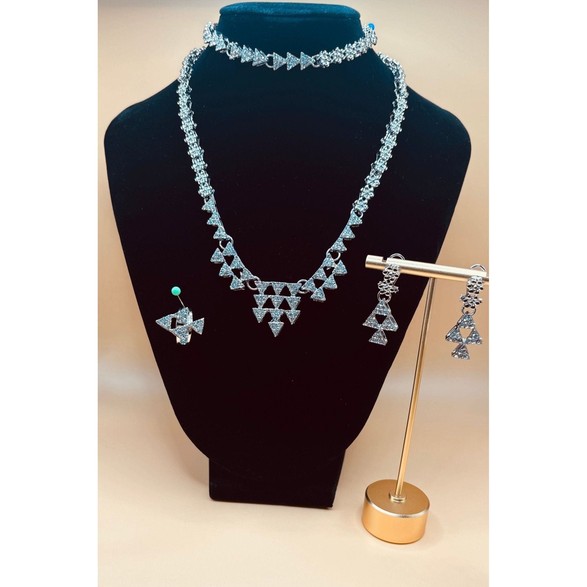 This Silver Crystal Necklace set showcases a beautifully designed triangle silver set, adorned with sparkling crystals. Perfect for formal occasions, this set includes a bracelet, earrings, ring, and necklace, adding an elegant touch to any outfit. Elevate your style with this stunning jewelry set.